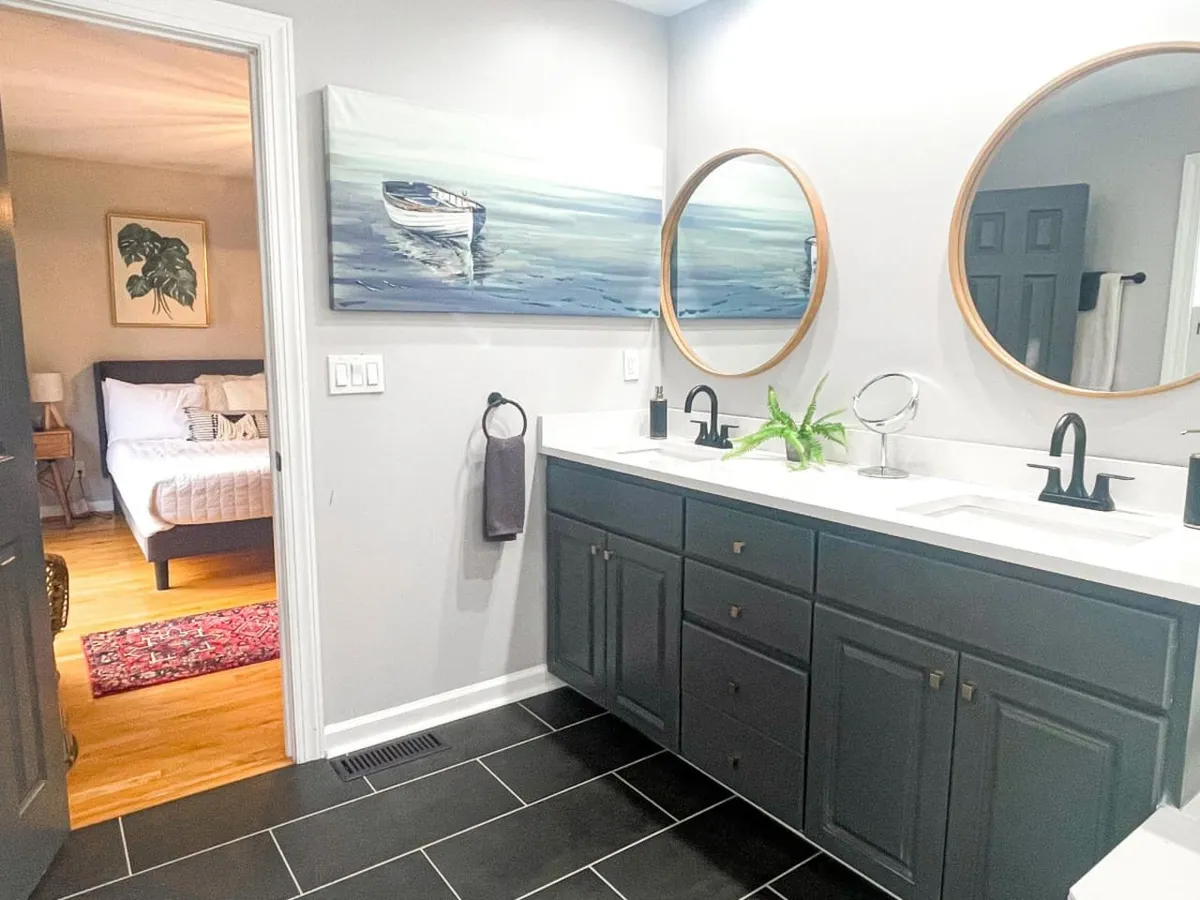 A bright, airy bathroom with a double vanity, round mirrors, artwork of a boat, and greenery. The modern fixtures and fresh style make it inviting for daily routines and self-care.