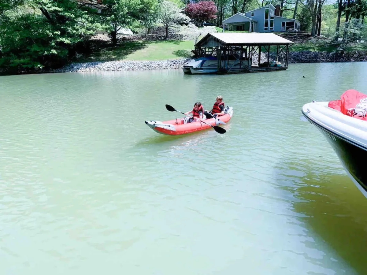 Two individuals in life jackets paddle a kayak on a calm lake, with a dock and lush greenery in the background. The scene radiates a sense of joy and adventure as they enjoy water activities together close to the home.