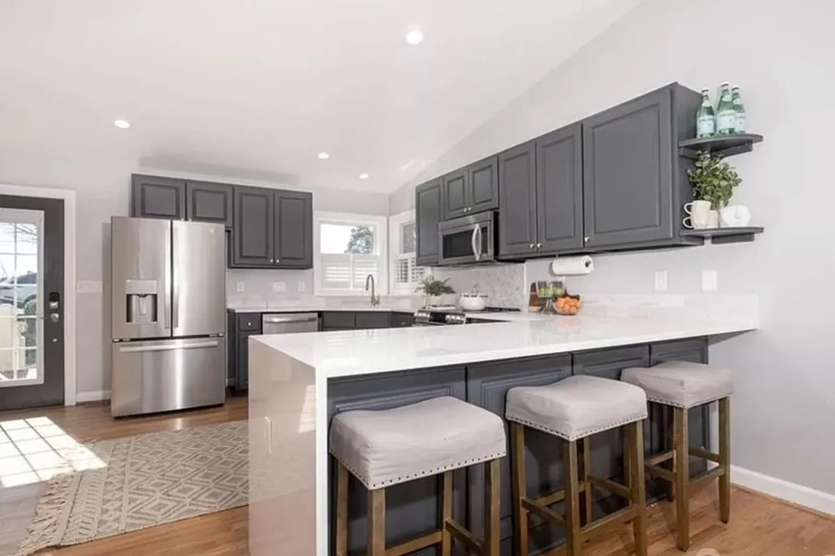 A modern kitchen with a large island, sleek stainless steel appliances, and gray cabinetry basking in sunlight. The open design encourages interaction and is ideal for preparing group meals or hosting casual brunches.