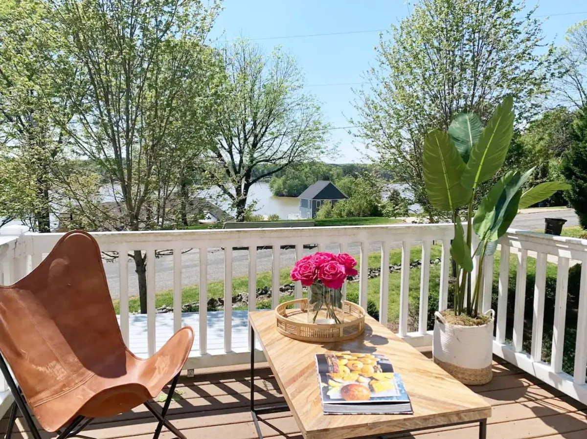 A tranquil outdoor seating area with a wooden table topped with flowers, a leather chair, and a picturesque view of the lake. The setting is ideal for morning coffee or relaxing with pets, highlighting easy access to outdoor spaces.