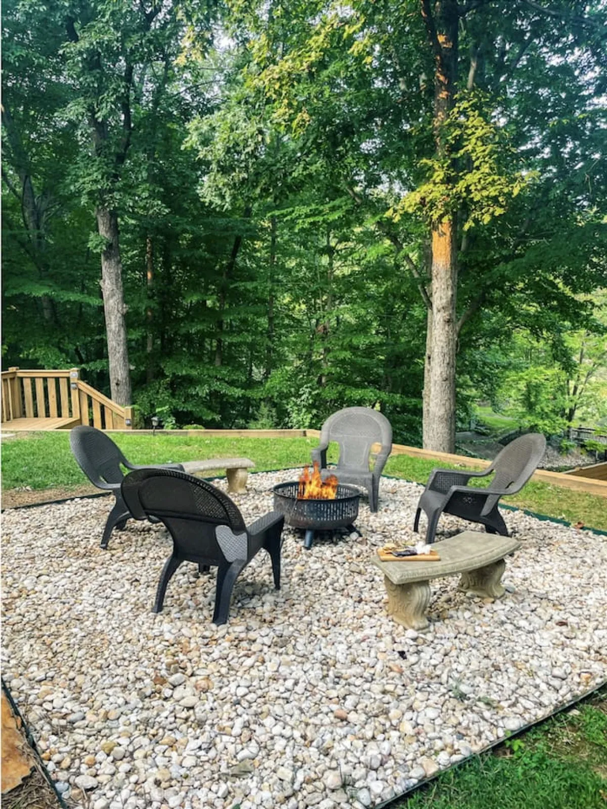 A cozy fire pit area is surrounded by comfortable chairs and stone benches amidst a wooded setting. The warm glow of the fire invites families to gather, roast s'mores, and share stories under the stars.