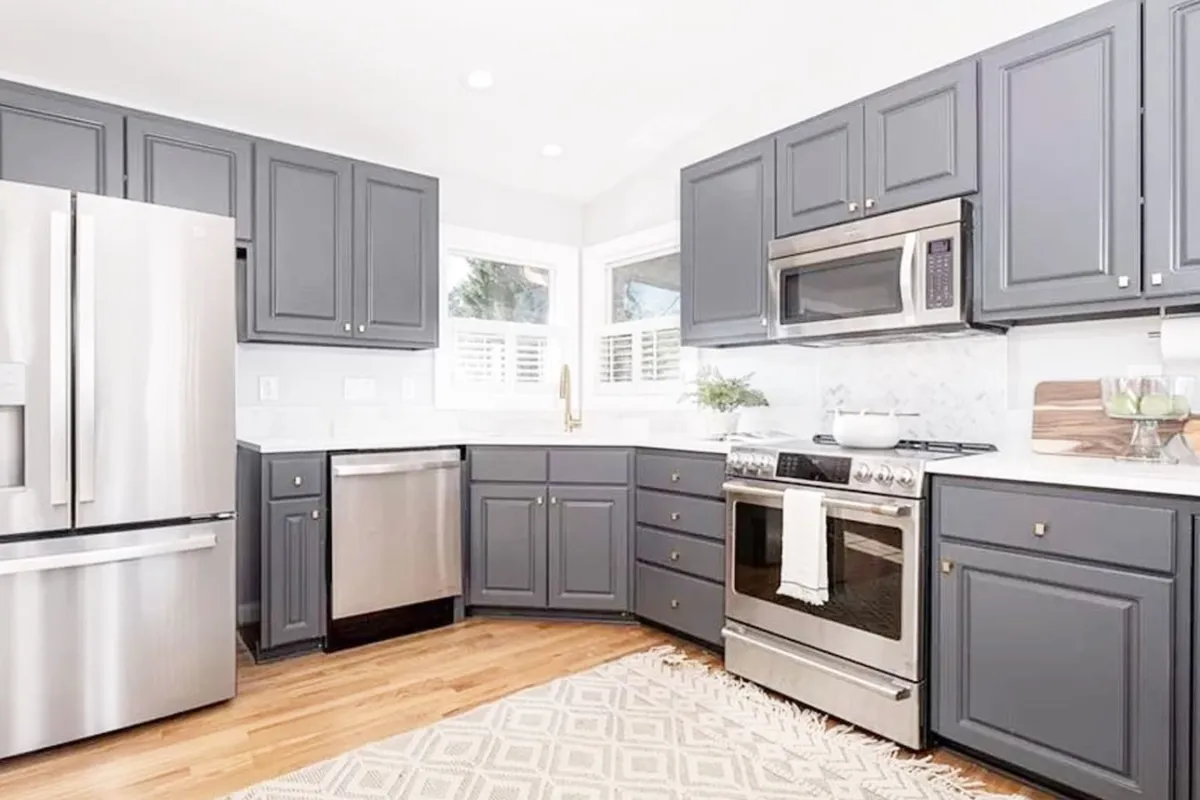A modern kitchen with stainless steel appliances, sleek gray cabinetry, marble countertops, and decorative accents, all bathed in natural light. The setting suggests a fresh, clean, and well-maintained environment.