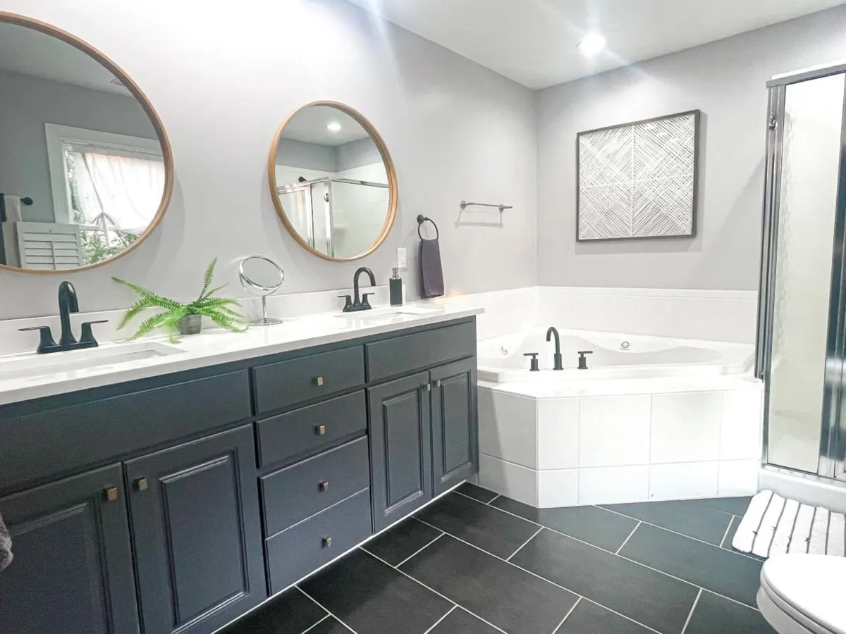 A sophisticated bathroom featuring a double vanity with dark cabinets, circular mirrors, a jacuzzi jetted tub, and a shower enclosure. The space is styled with elegant finishes, evoking a spa-like ambiance.