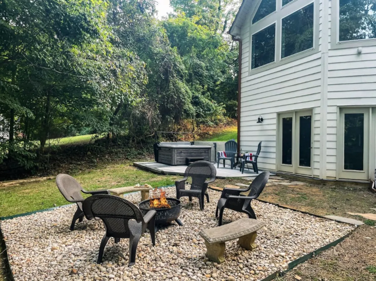 A cozy exterior living space featuring a fire pit, inviting seating area, and a hot tub nestled among greenery. The area invites couples to unwind, stargaze, and enjoy warm fireside chats after a day of adventure.