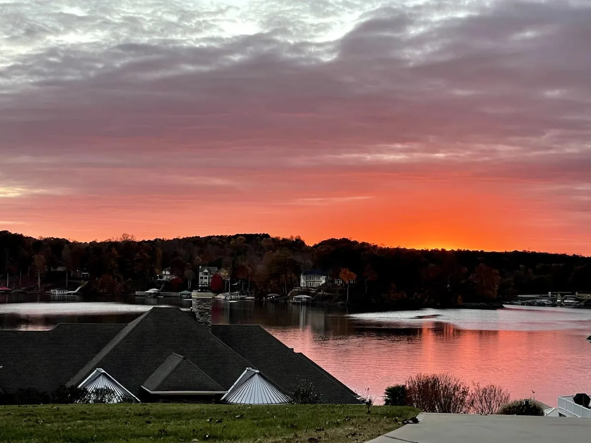 A breathtaking sunset over Lake Norman, with golden reflections shimmering on the calm water and autumn foliage framing the serene view. The scene radiates tranquility and natural beauty, inviting quiet moments together.